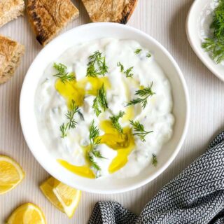 Tzatziki sauce topped with fresh dill and olive oil with lemons, dill and pita bread for dipping.