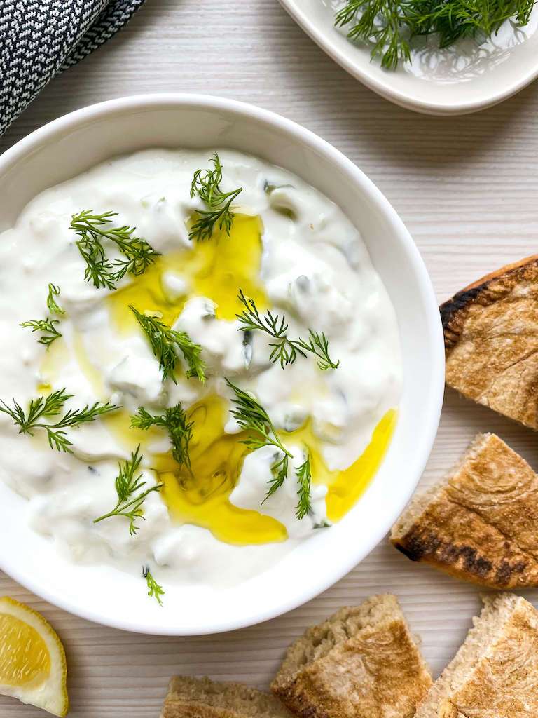 Garlic tzatziki sauce topped with fresh dill and olive oil with lemons, dill and pita bread for dipping.