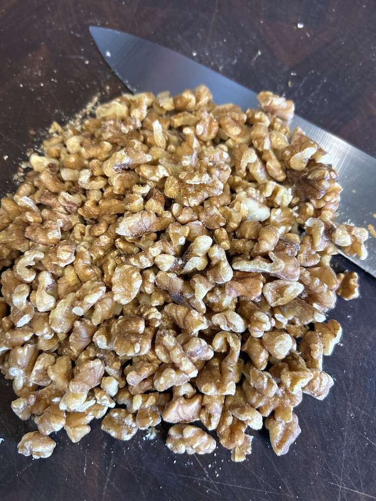 Chopped Walnuts on a wooden cutting board with a knife.