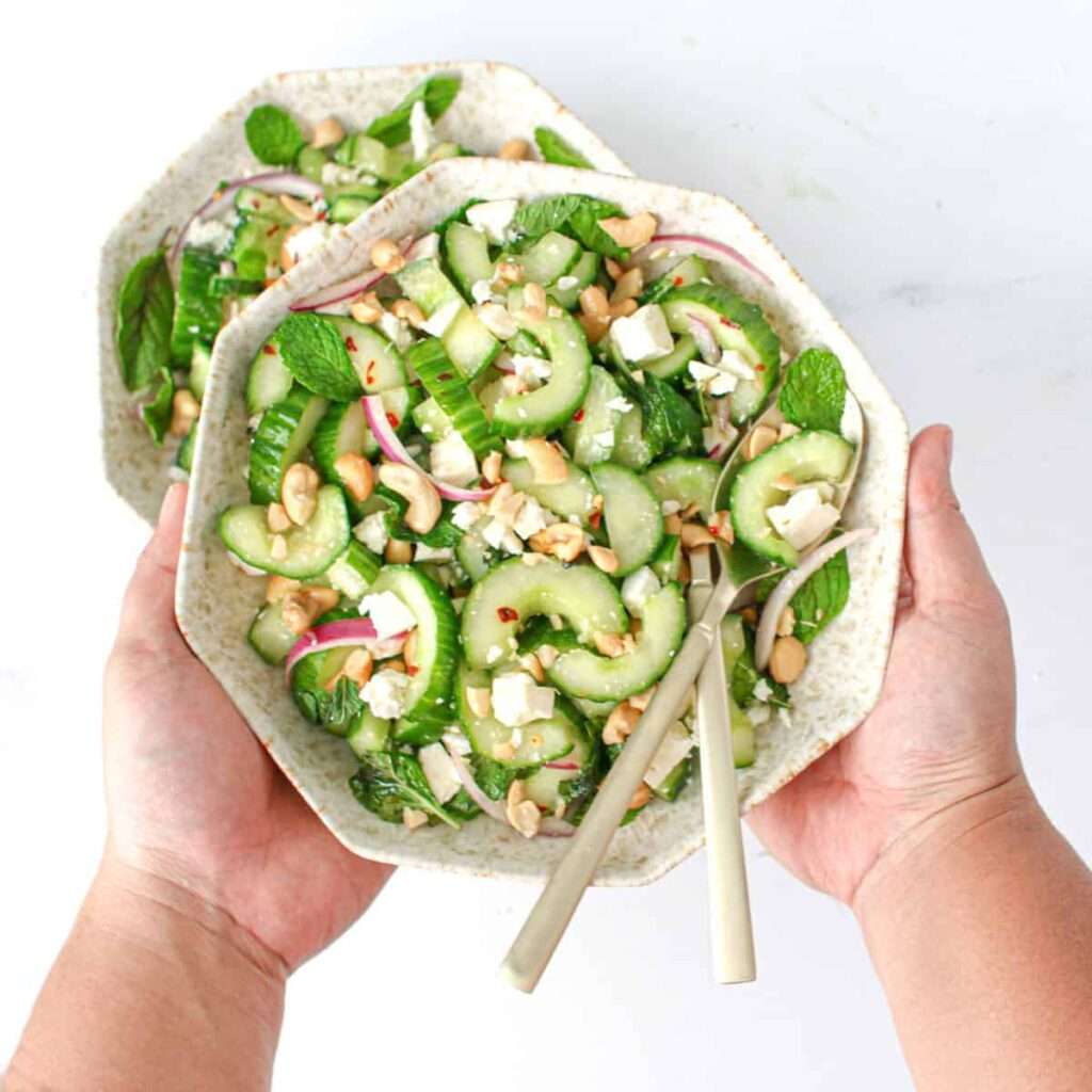 10 Fun Facts About Cucumbers Cucumber mint feta salad in a bowl with a fork and spoon being passed across a table.