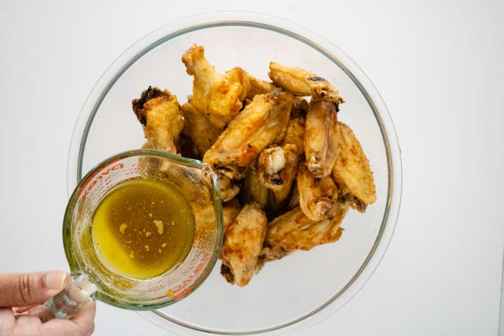 Pouring the Buffalo Wild Wings lemon pepper sauce over the wings in a large mixing bowl.