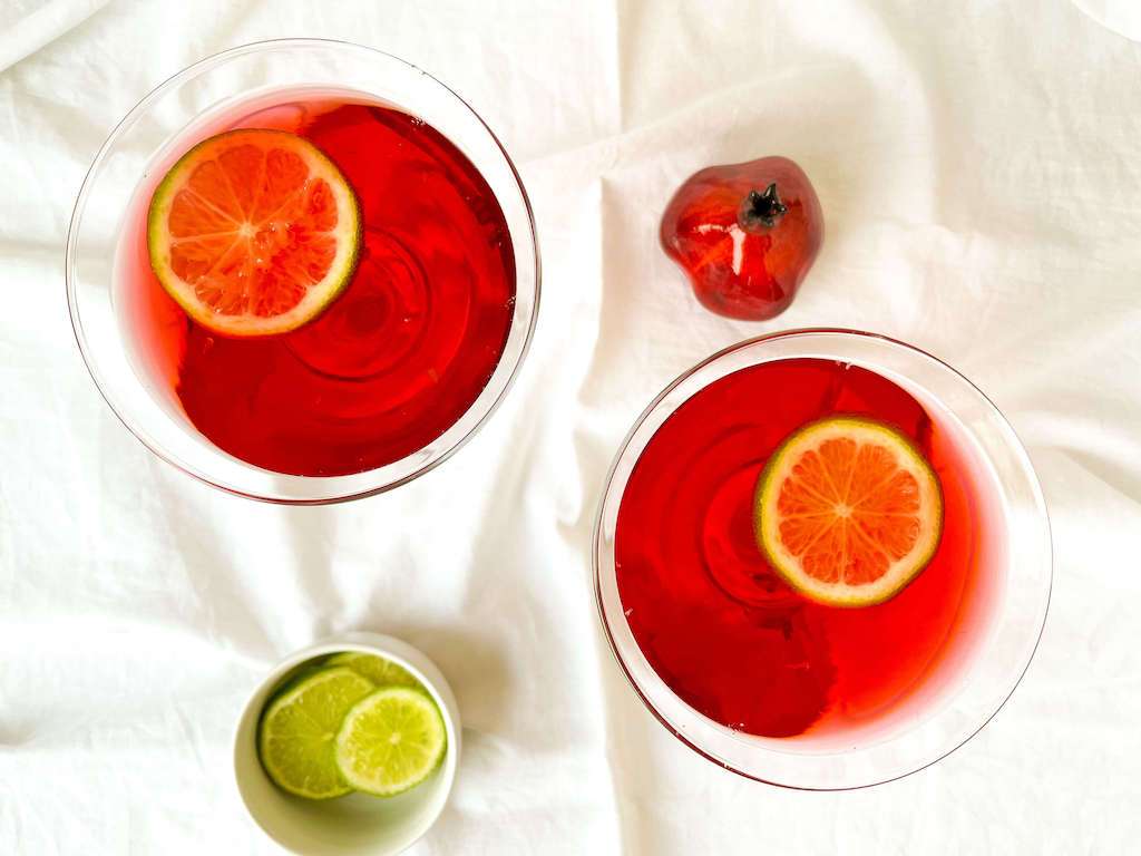 Two pom cosmo drinks in martini glasses with a bowl of limes for garnish.