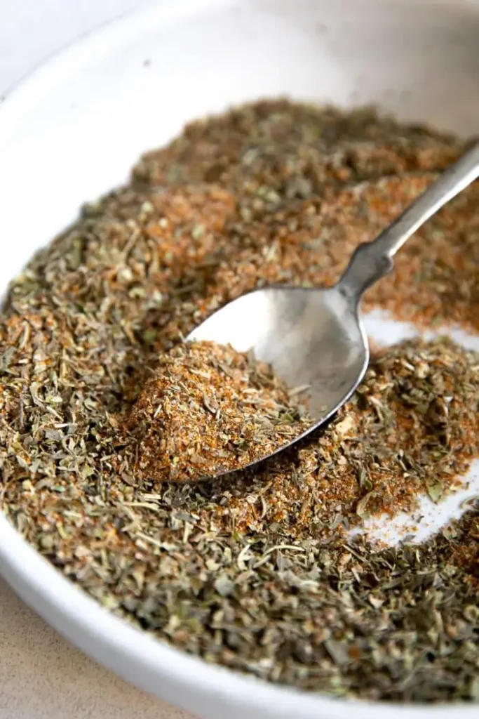 Spoon scooping homemade herb and spice blend in white bowl