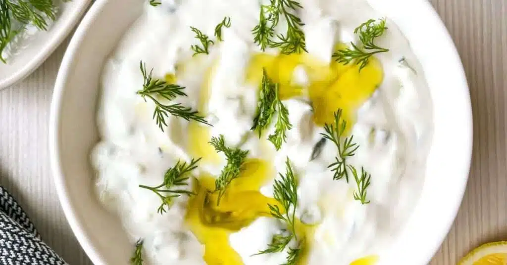 Tzatziki sauce topped with fresh dill and olive oil with lemons, dill and pita bread for dipping.