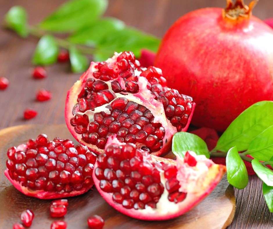 A pomegranate broken in thirds with a whole pomegranate in the background.