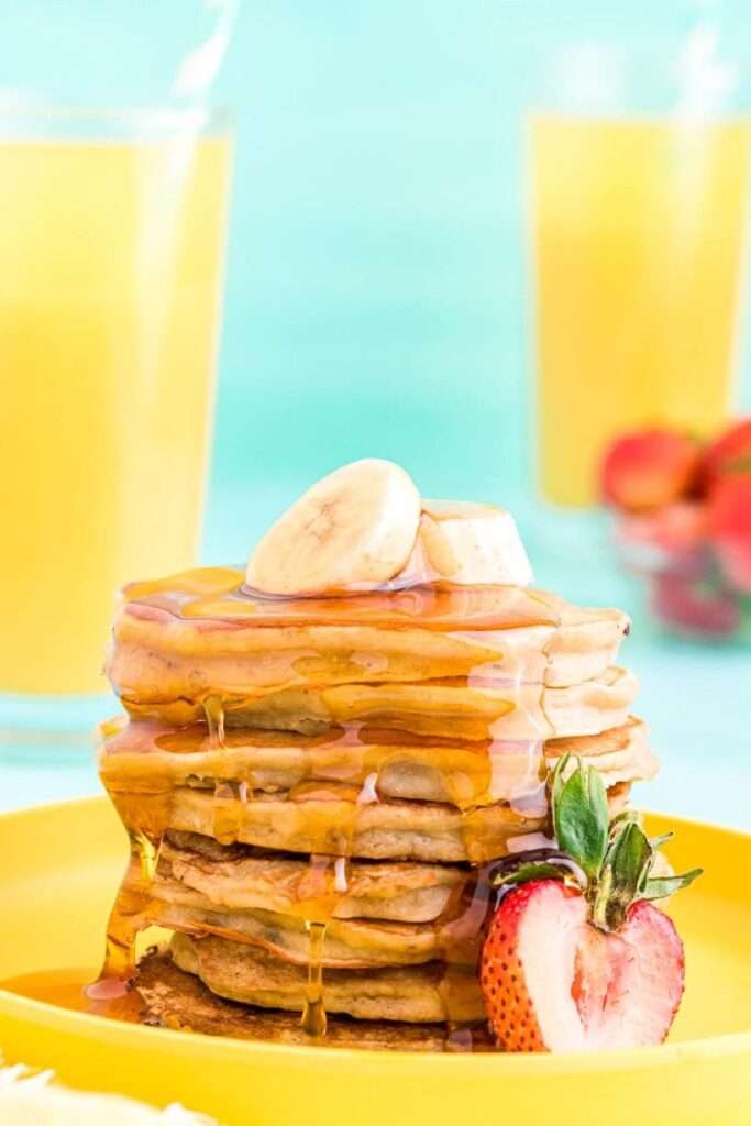 23 Fun Facts About Bananas Stack of banana pancakes with maple syrup, strawberry, and orange juice behind