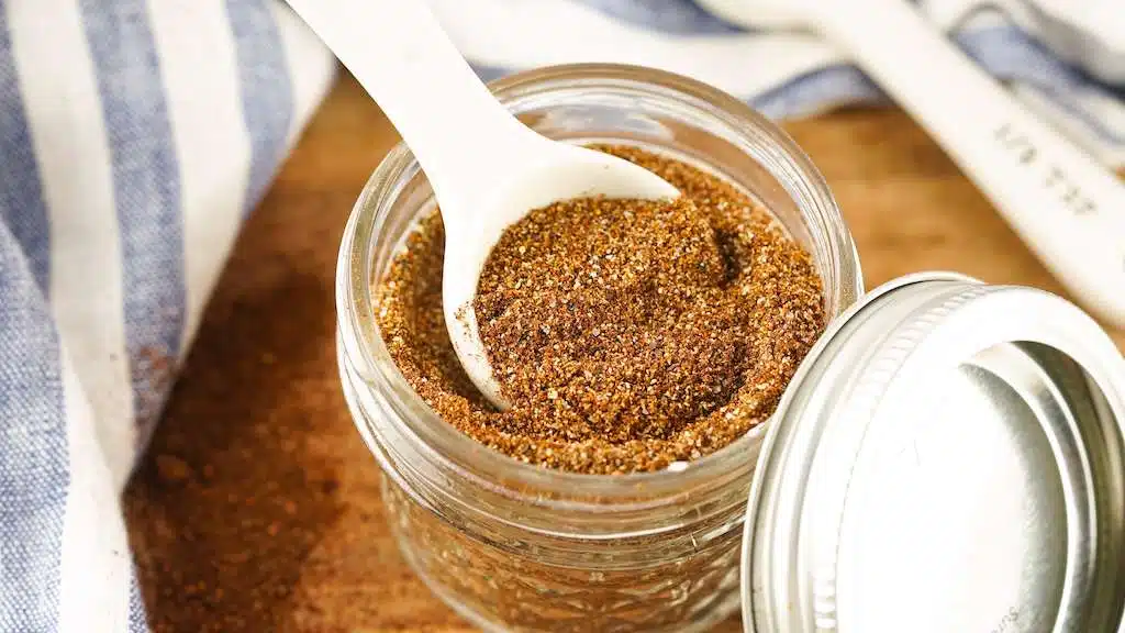 Homemade spice blend in a glass jar with spoon and lid on table
