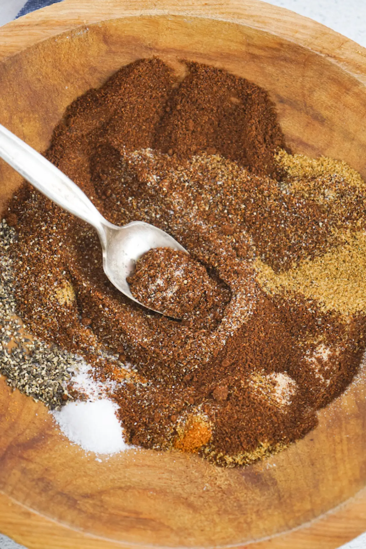 Homemade taco seasoning blend in a wooden bowl with spoon, featuring chili, cumin, pepper, and salt