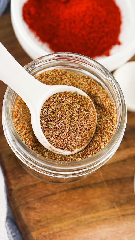 Homemade taco seasoning in a mason jar with a white spoon.