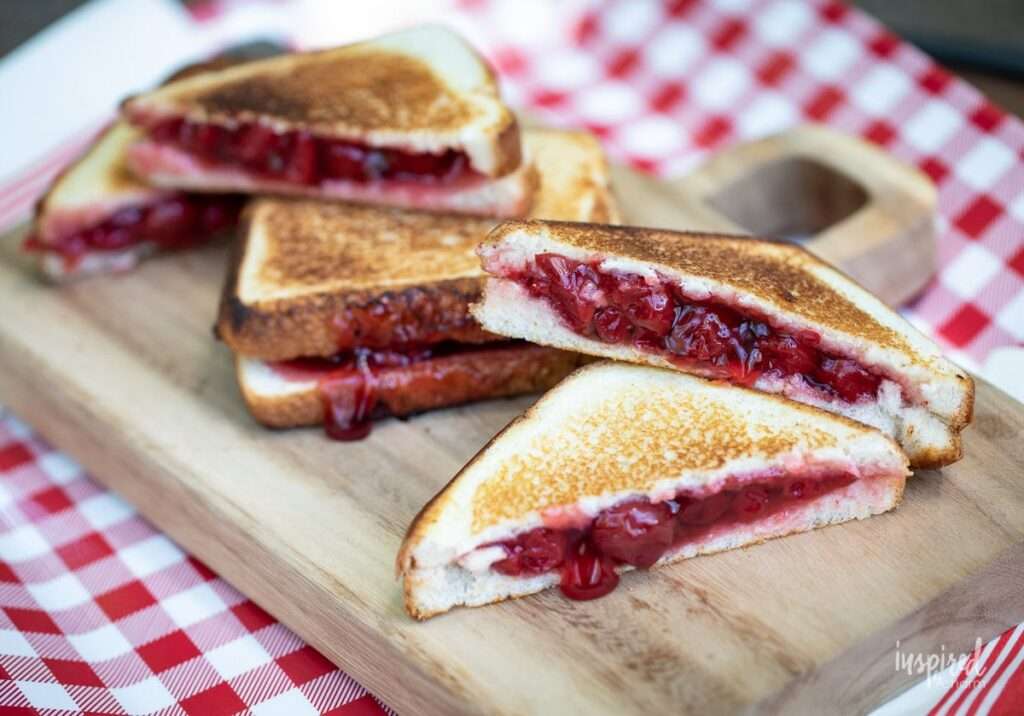 13 Pie Iron Recipes - Sweet & Savory Grilled cherry pie sandwiches on wooden board, picnic tablecloth