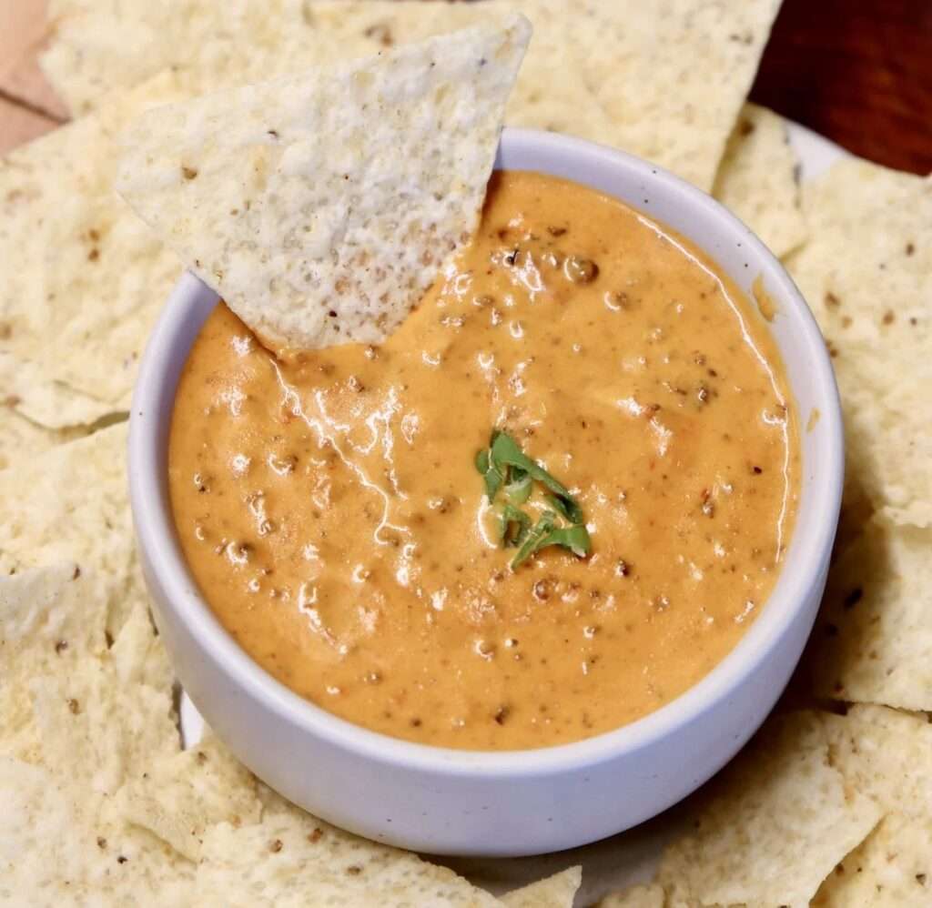 12 Creative Leftover Chili Recipes Creamy queso cheese dip in a white bowl with tortilla chips and green garnish