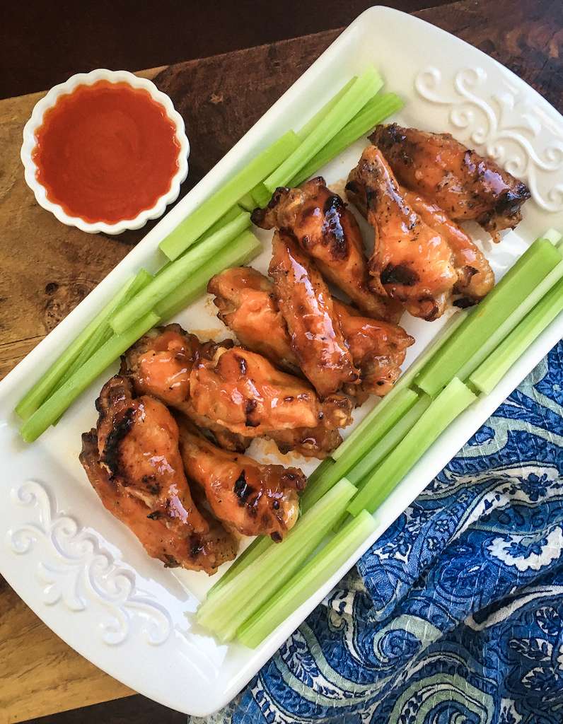 Instant Pot Buffalo Chicken Wings on a white plate with celery sticks and extra buffalo sauce for dipping.