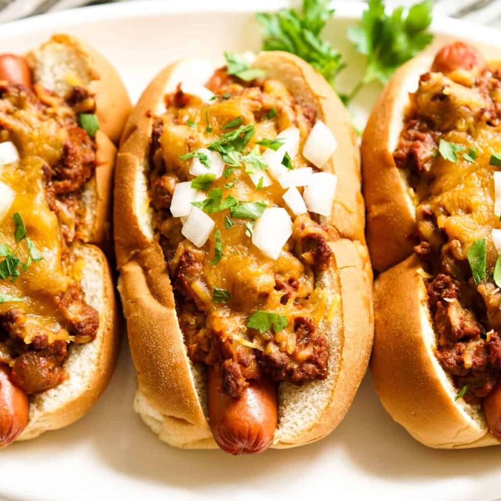 12 Creative Leftover Chili Recipes Chili cheese hot dogs topped with onions and parsley on buns
