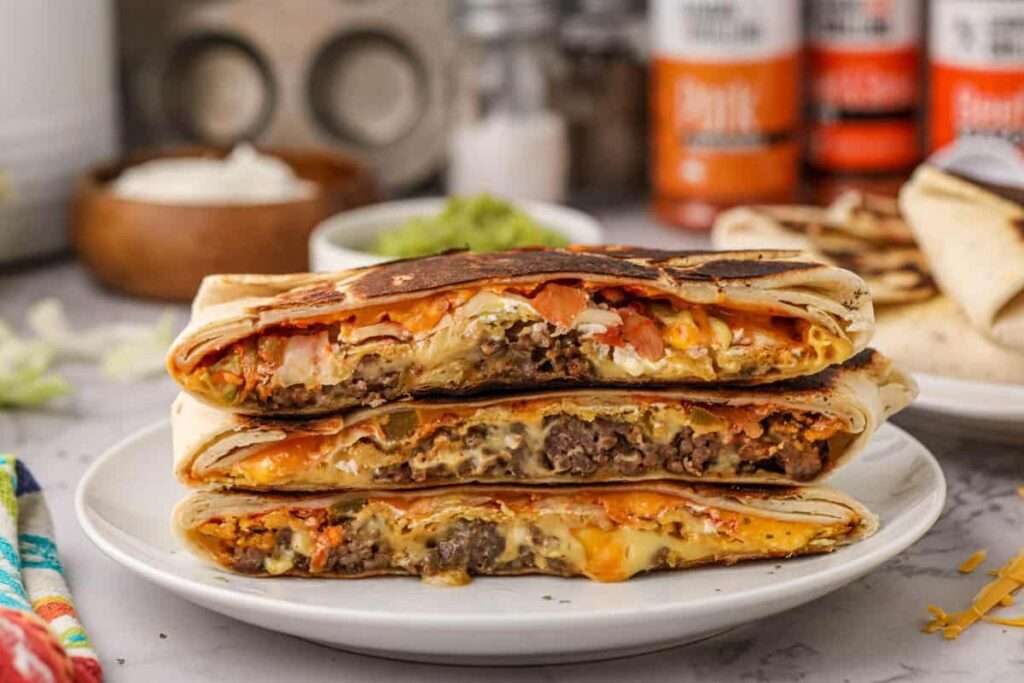 15 Best Blackstone Recipes Stacked grilled beef and melty cheese crunchwrap halves on plate