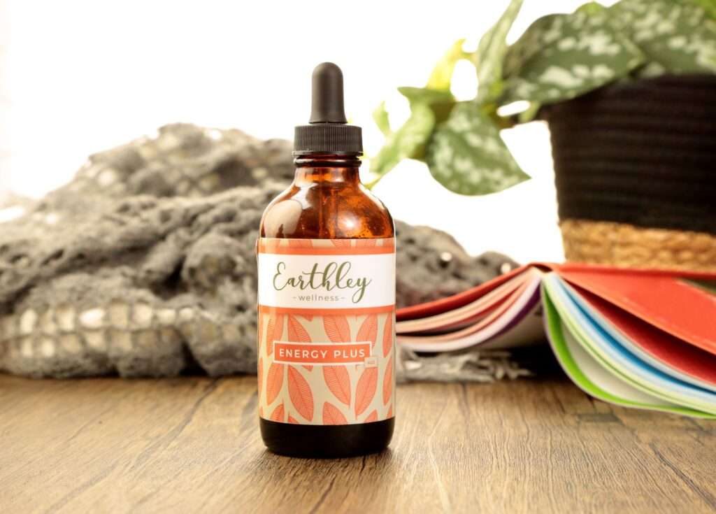 A bottle of Energy Plus iron supplement on a wooden table with a book, a blanket and a plant in the background.