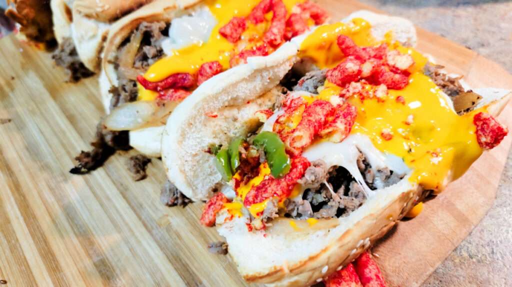 15 Best Blackstone Recipes Philly cheesesteak hoagie topped with melted cheese and Flamin' Hot Cheetos