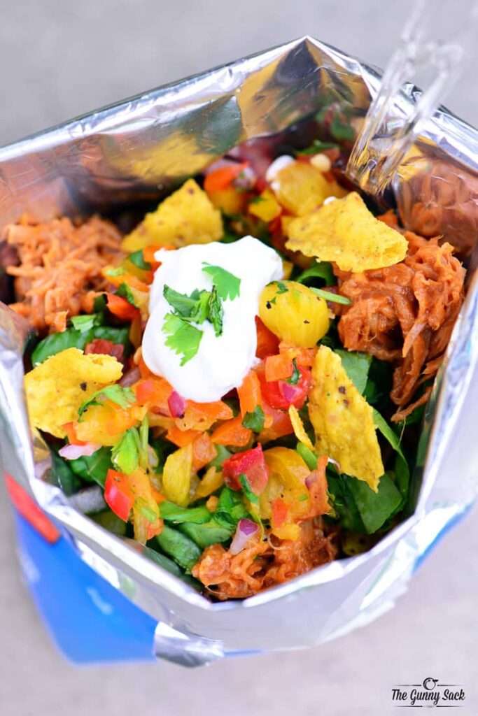 14 Walking Recipes Perfect for Camping Walking taco in a chip bag with shredded chicken, fresh salsa, and sour cream