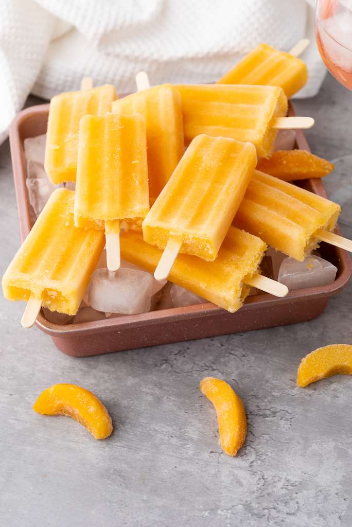 20+ Single Serve Desserts Simple To Make Peach Rose Wine Popsicles on a copper cookie sheet with a glass of peach rose wine and a white towel in the background.