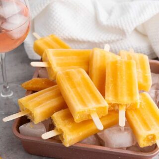 Peach Rose Wine Popsicles on a copper cookie sheet with a glass of peach rose wine and a white towel in the background.