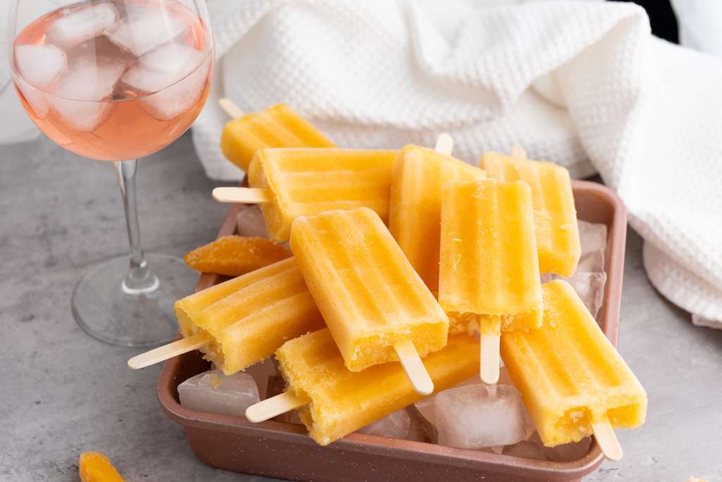 Peach Rose Wine Popsicles on a copper cookie sheet with a glass of peach rose wine and a white towel in the background.