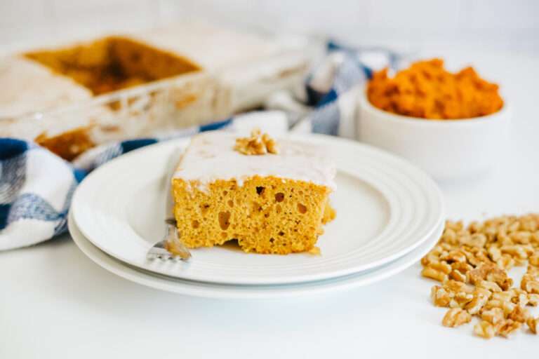 A slice of Pumpkin Honey Bun Cake on a white plate with walnuts, pumpkin purée and the cake pan in the background.