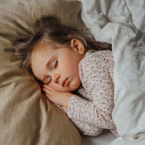 A little girl sleeping with her hands tucked under her head.