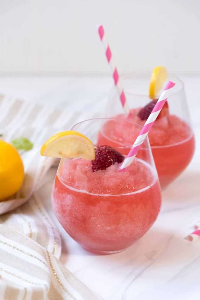 11 Refreshing Wine Slushie Recipes for Summer Two strawberry lemonade slushies with lemon wedges and pink straws.