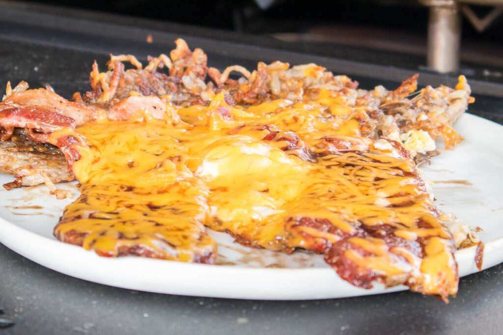15 Best Blackstone Recipes Melted cheddar over bacon, hash browns, and eggs on a breakfast plate