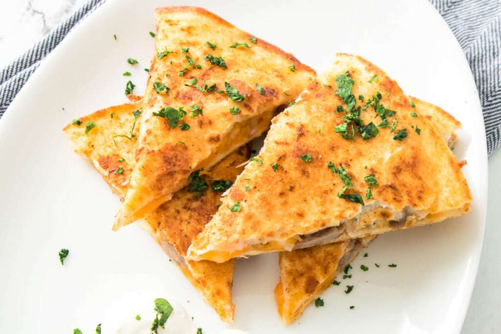 15 Best Blackstone Recipes Crispy cheese quesadilla slices with melted cheddar and cilantro on a white plate