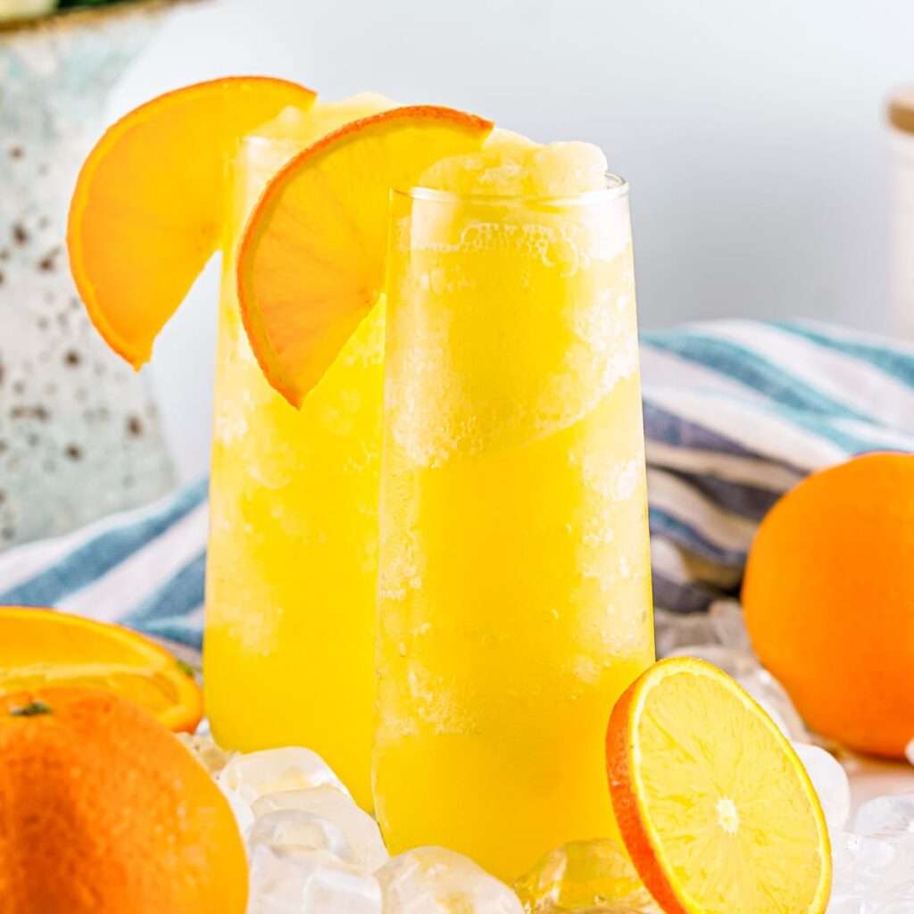 11 Refreshing Wine Slushie Recipes for Summer Two frozen orange mimosas garnished with orange slices on ice