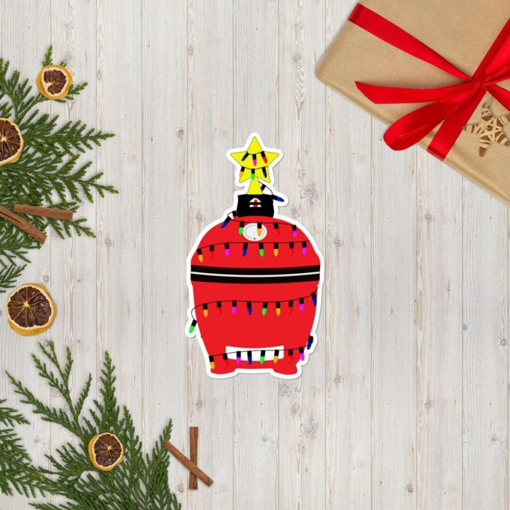 14 Unique Kamado Joe Gifts for Your Grill Master Christmas flat lay with gift wrapped in red ribbon, evergreen sprigs, and red ornament sticker on wood background