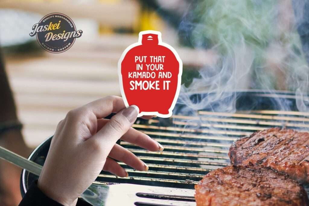 14 Unique Kamado Joe Gifts for Your Grill Master Hand holding kamado BBQ sticker by smoking grill with sizzling burgers