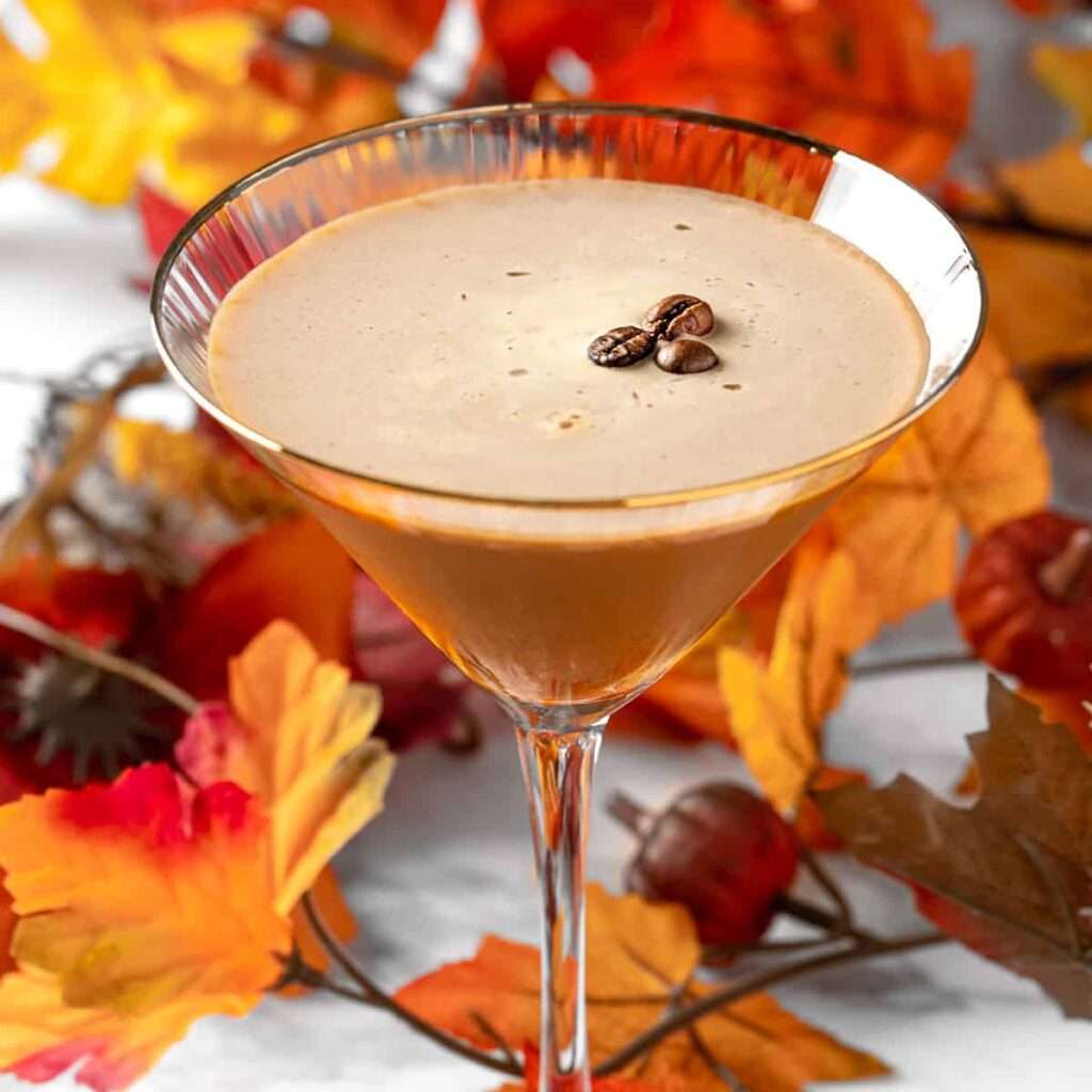 11 Delicious Pumpkin Cocktails to Try This Fall A pumpkin espresso martini in martini glass garnished with espresso beans and surrounded by Fall leaves.