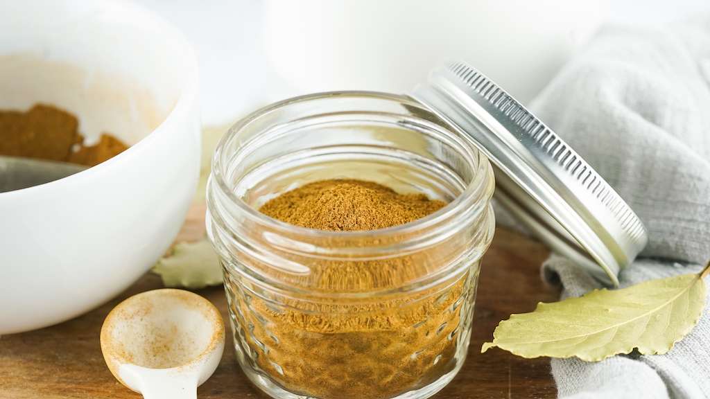 Homemade pumpkin pie spice mix in a small mason jar with measuring spoon.