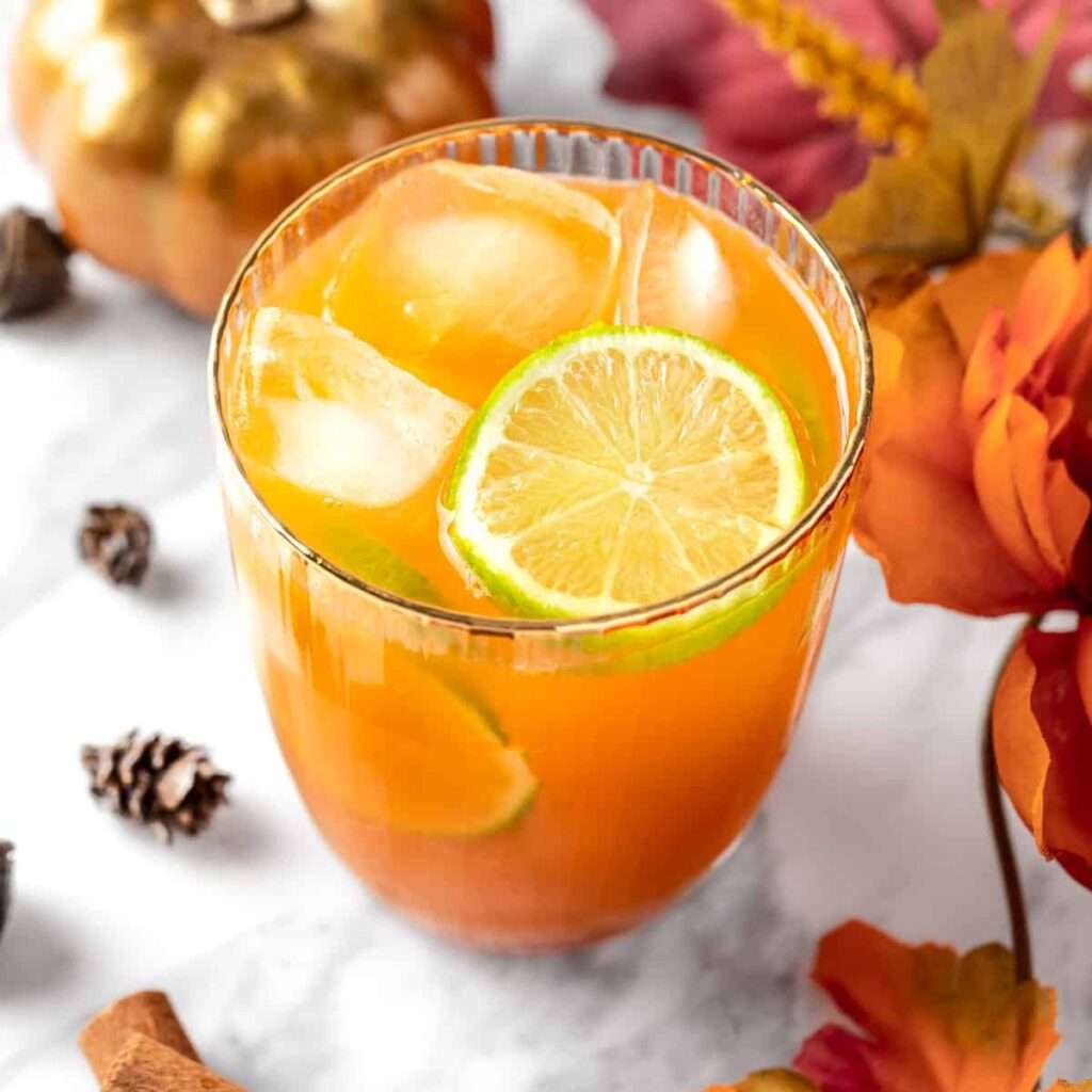 11 Delicious Pumpkin Cocktails to Try This Fall A pumpkin spice margarita in a glass surrounded by Fall themed decorations.