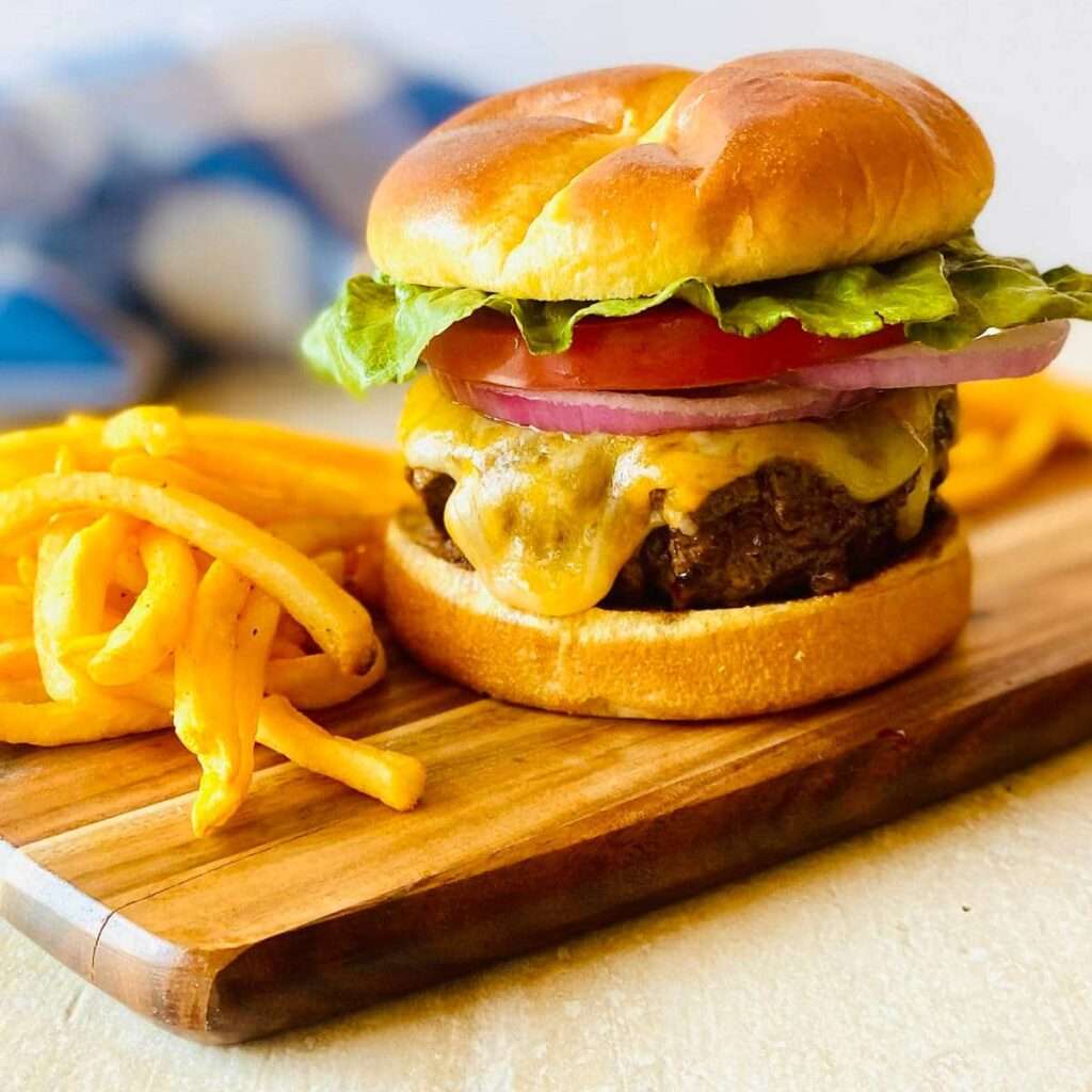 15 Best Blackstone Recipes Juicy cheeseburger with melted cheddar, lettuce, tomato, onion on brioche bun with curly fries.