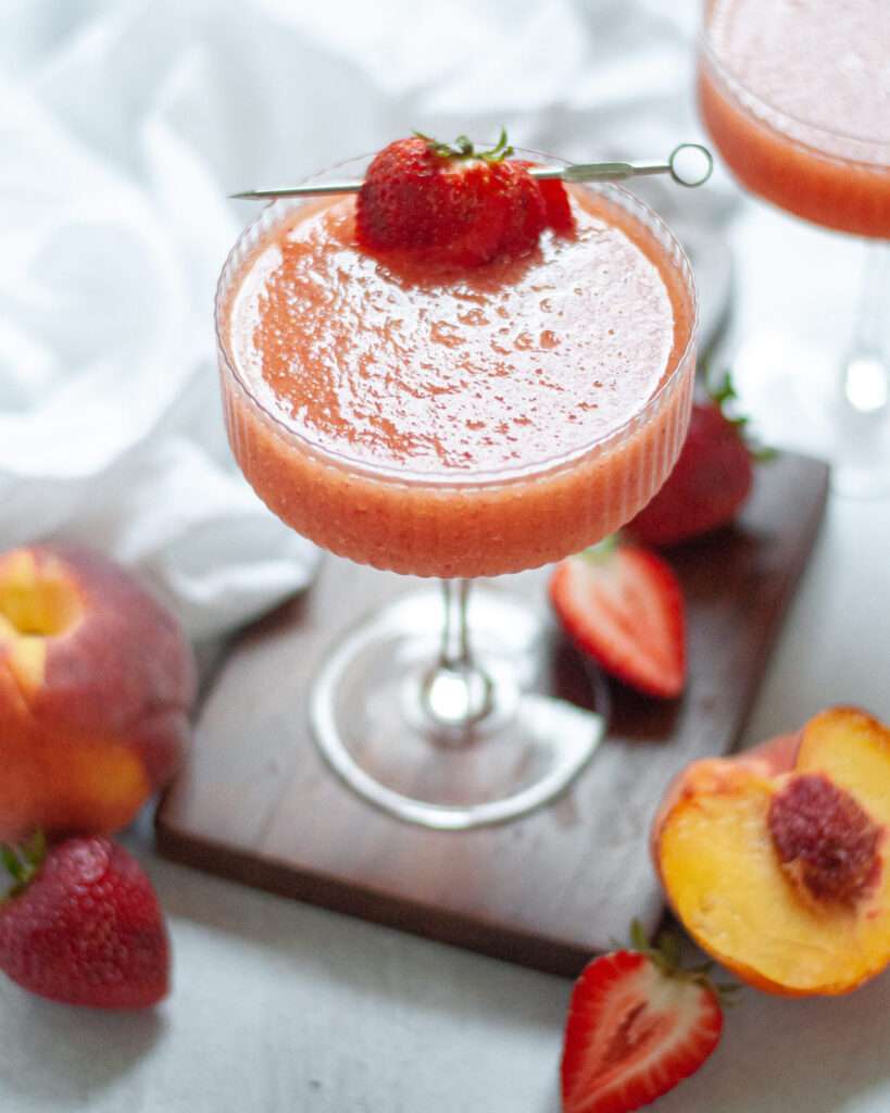 11 Refreshing Wine Slushie Recipes for Summer Strawberry peach frozen cocktail in a coupe glass, garnished with fresh strawberry