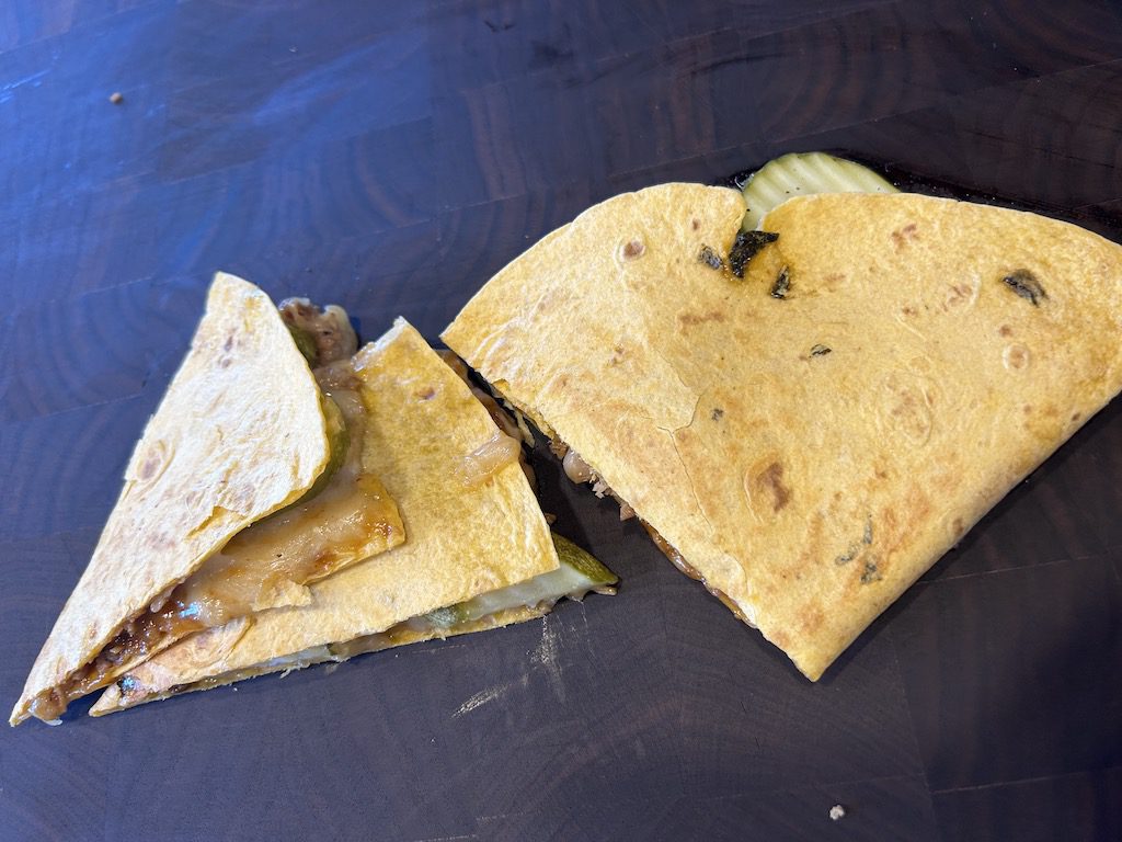 A cuban sandwich quesadilla sliced into servings on a wooden cutting board.