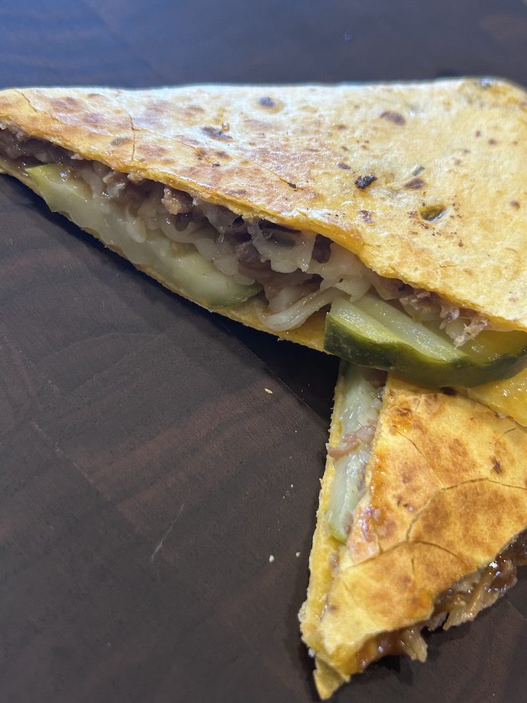 Two slices of a cuban quesadilla on a wooden cutting board.