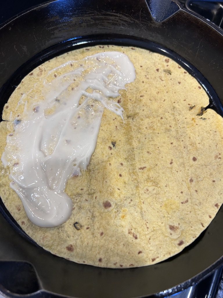 A jalenpeno cheddar tortilla with garlic aioli spread on one half in a cast iron skillet on the stove.