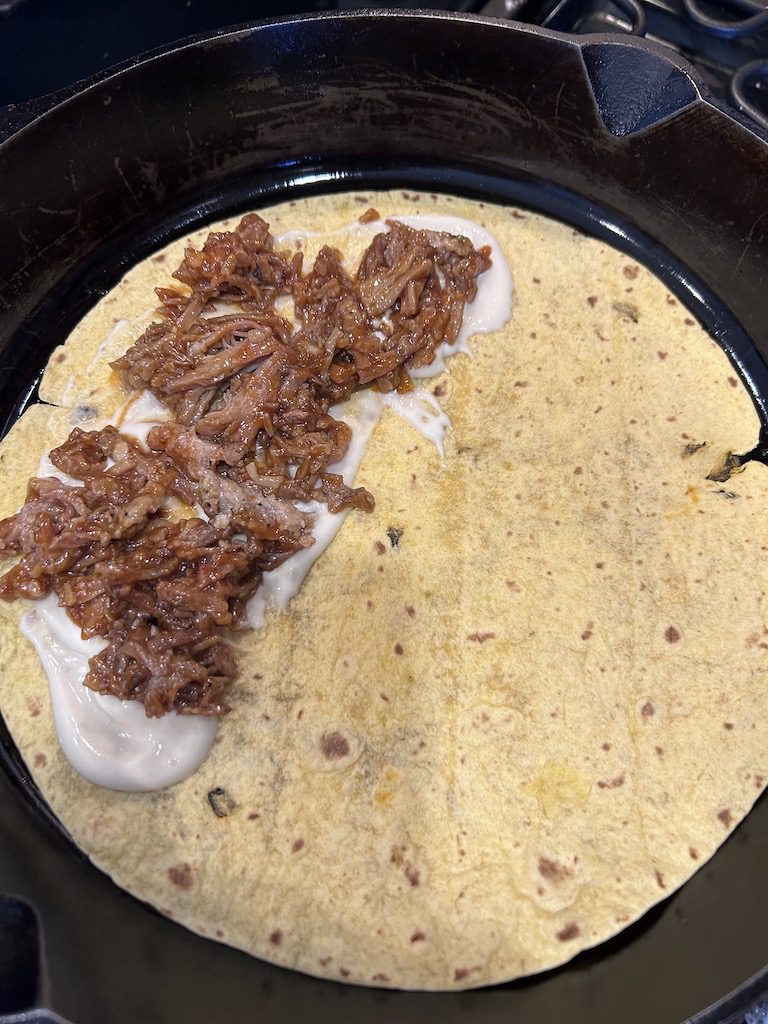 The jalapeno cheddar tortilla with garlic aioli in the cast iron skillet with shredded Barbeque pork on top.