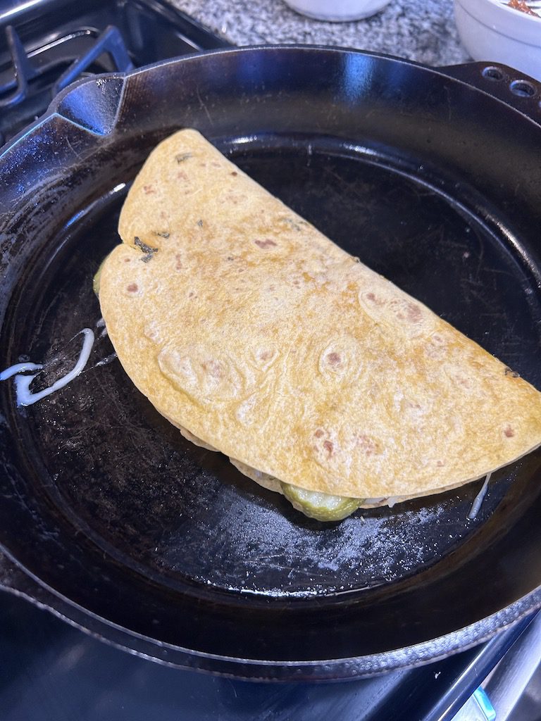 The cuban quesadilla with the filling ingredients folded in half in a cast iron skillet.