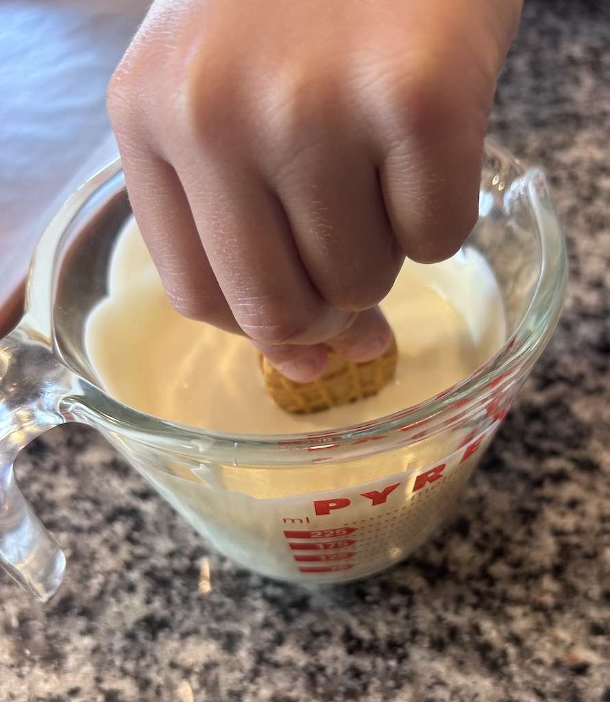 Dipping a nutter butter cookie into melted white almond bark in a glass measuring cup.