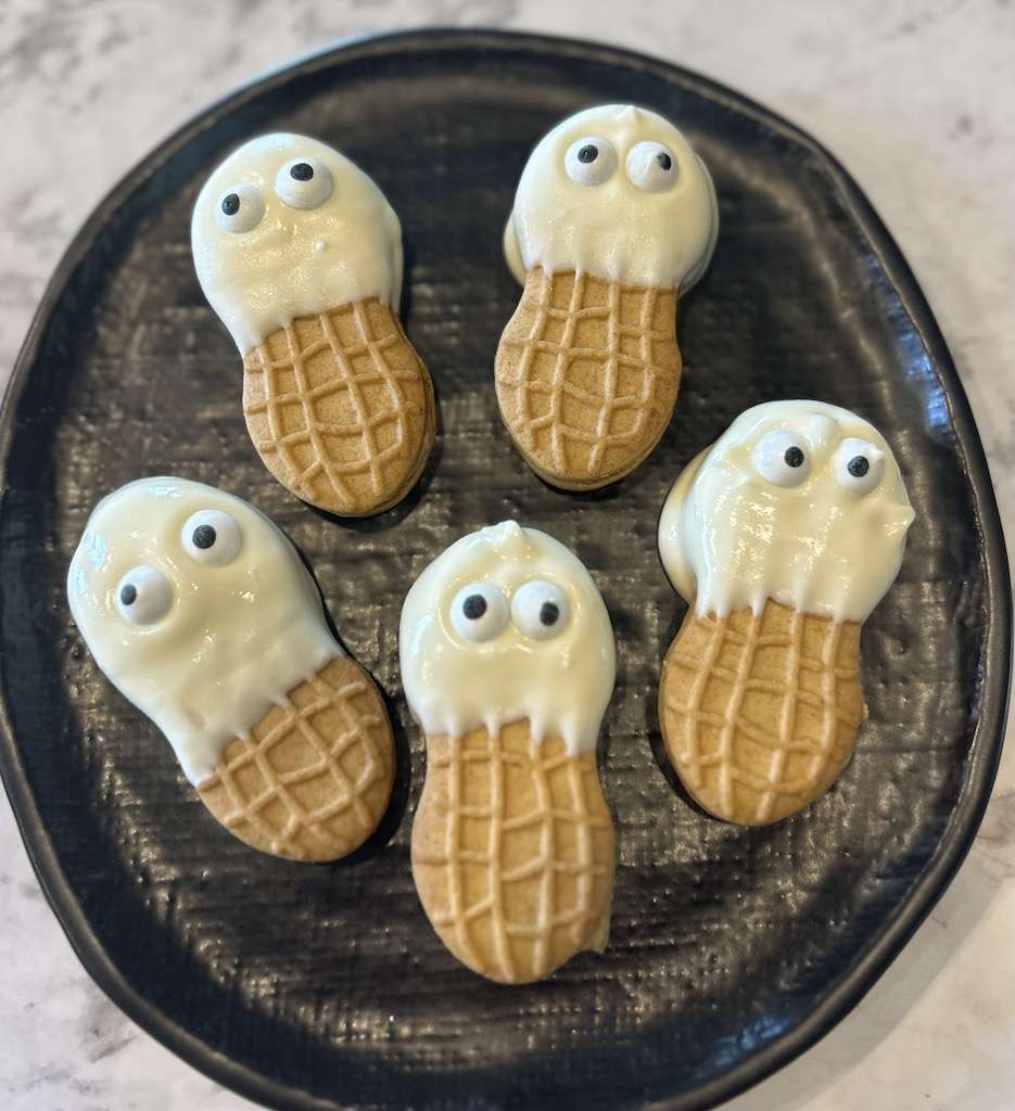 Five nutter butter ghost cookies on a black plate on a marble counter top.