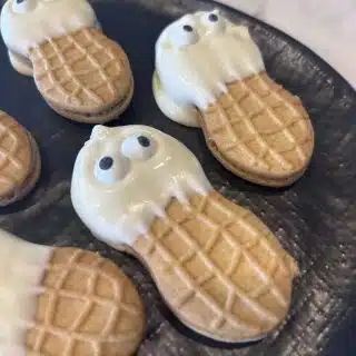 A few ghost cookies on a black plate on a marble counter top.