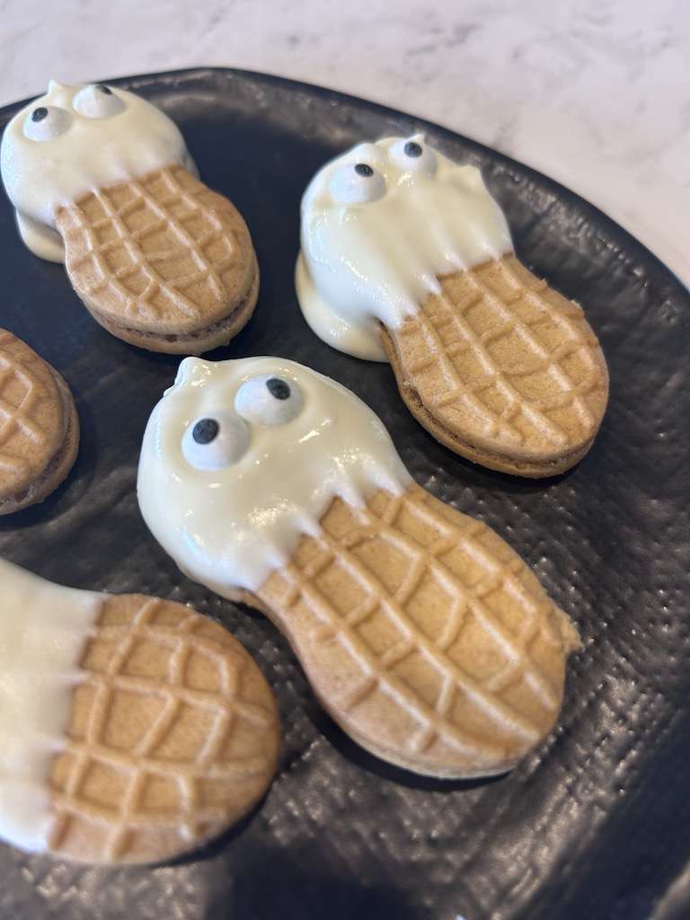 A few ghost cookies on a black plate on a marble counter top.