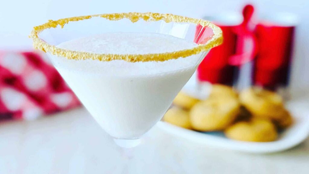 11 Christmas Cocktails with Baileys Creamy dessert cocktail in martini glass with graham cracker rim, cookies behind