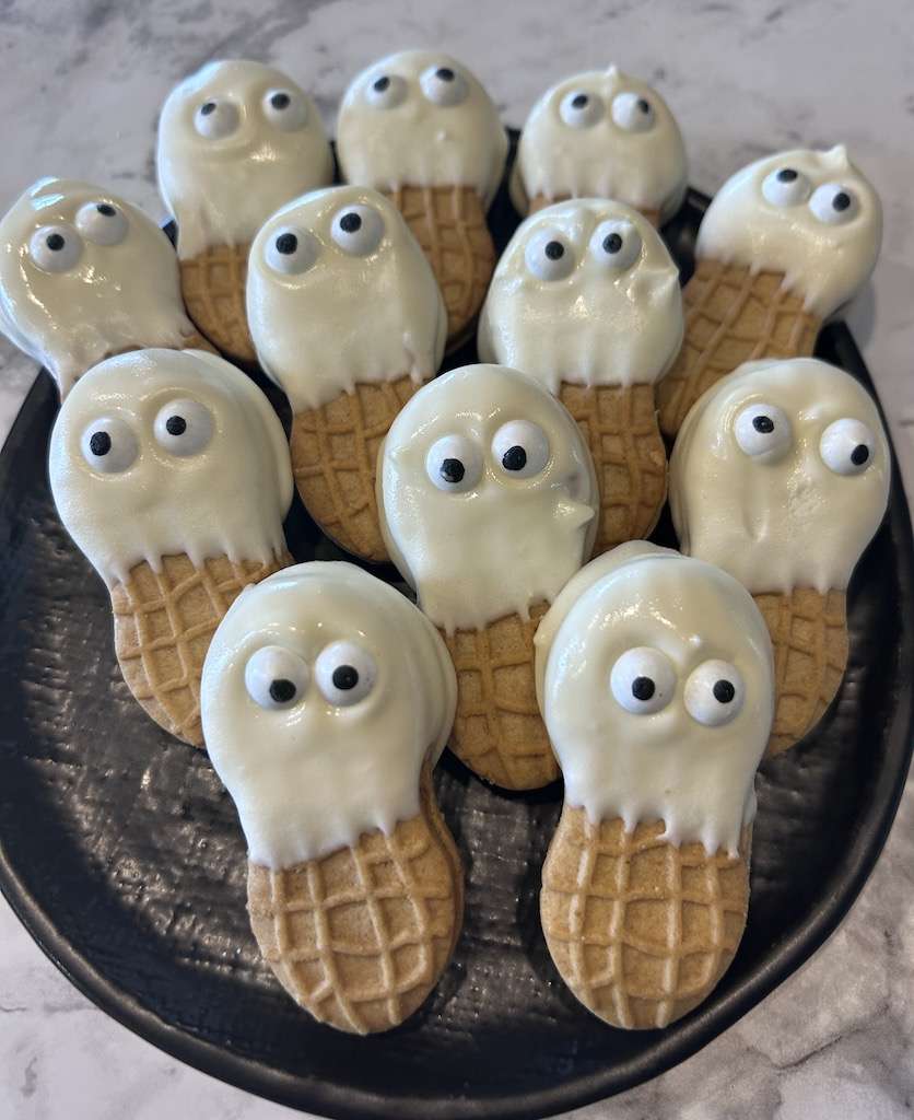 A black plate of 12 ghost cookies on a marble counter.