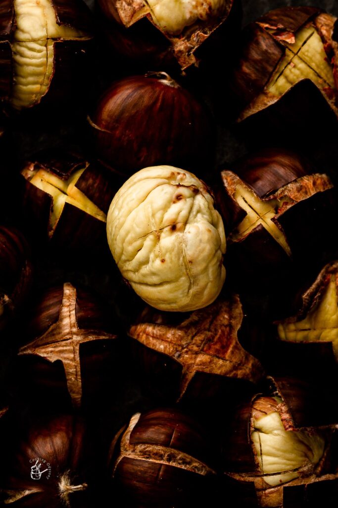 8 Traditional Christmas Flavors Close-up of roasted chestnuts with cracked shells and a peeled nut.