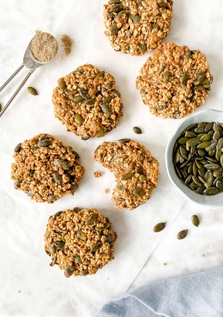 8 Traditional Christmas Flavors Healthy pumpkin seed oatmeal cookies on parchment, one with a bite